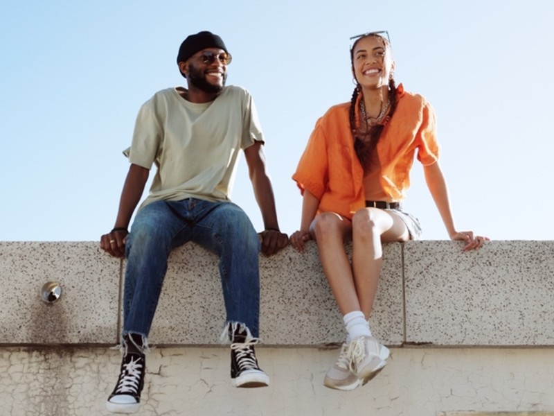 Two smiling young adults sit on a roof together