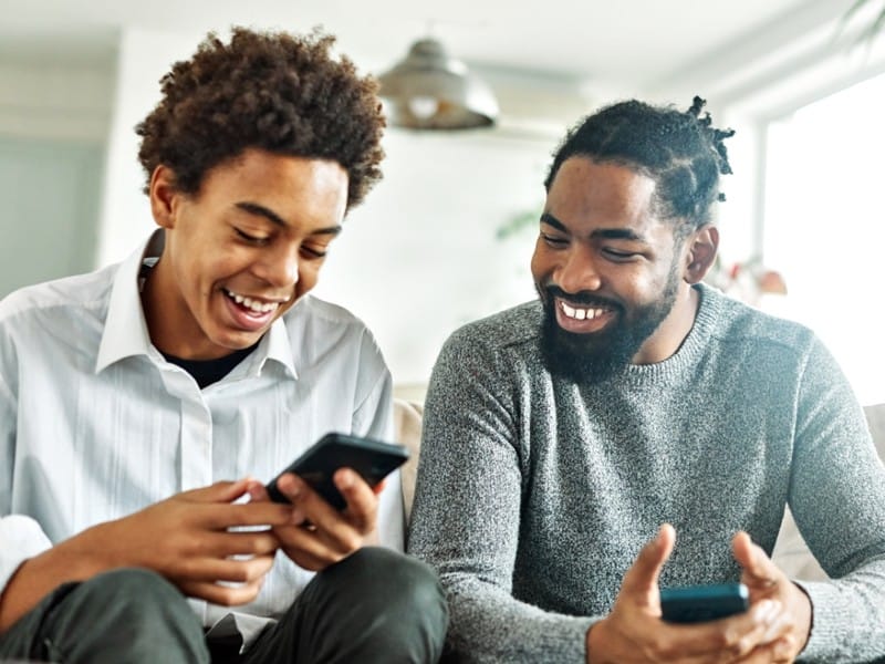 A youth and his mentor smile as they look at their phones together